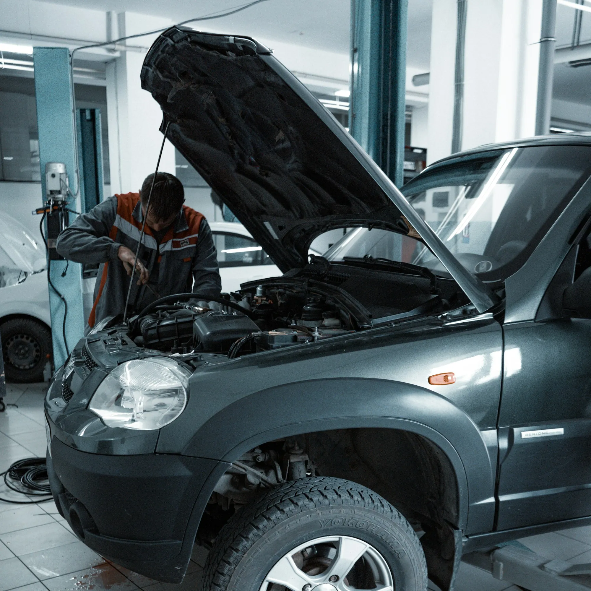 Mechanic working inside the engine bay of a grey SUV in a repair shop
